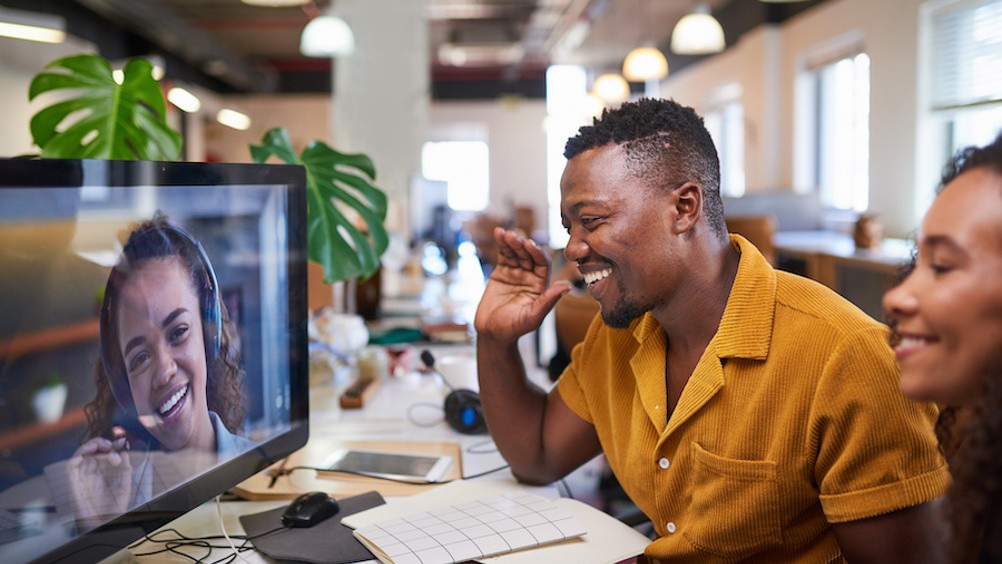 A Black man waves to his colleague on a video call from his office. High quality photo